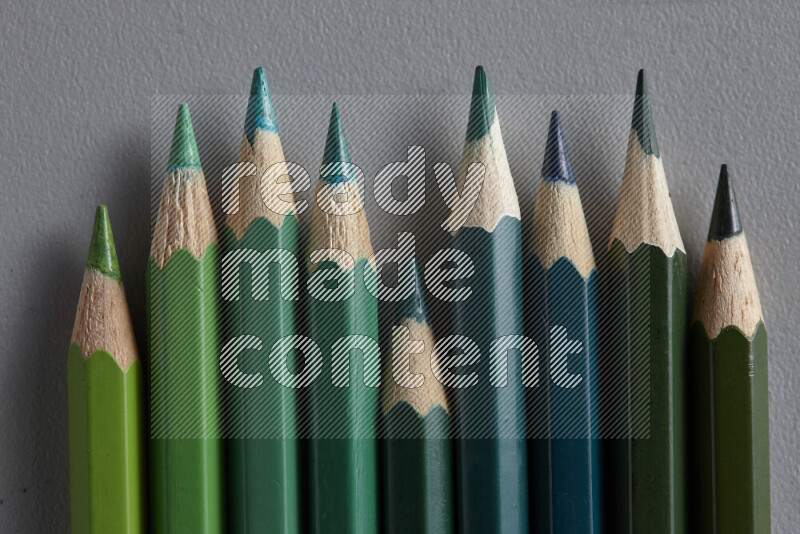 A collection of colored pencils arranged showcasing a gradient of green hues on grey background