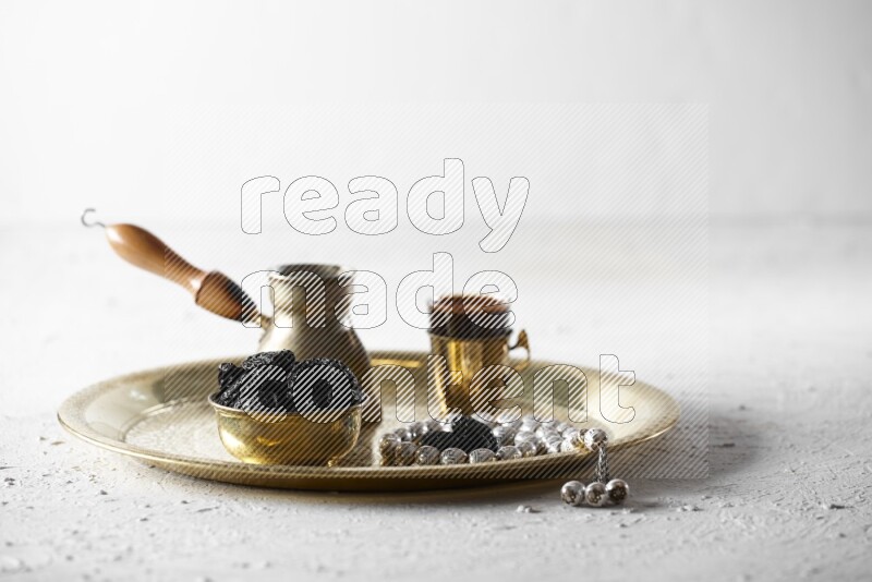 Dried plums in a metal bowl with coffee and prayer beads on a tray in a light setup