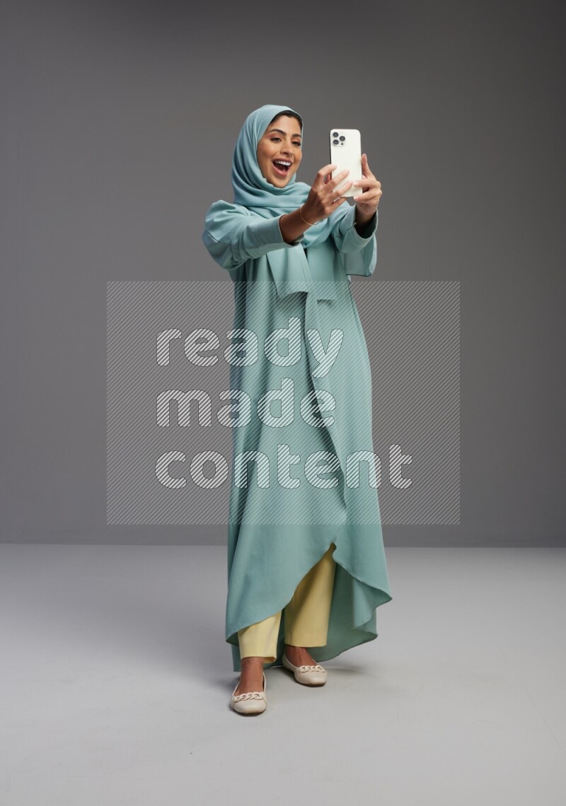 Saudi Woman wearing Abaya standing taking selfie on Gray background
