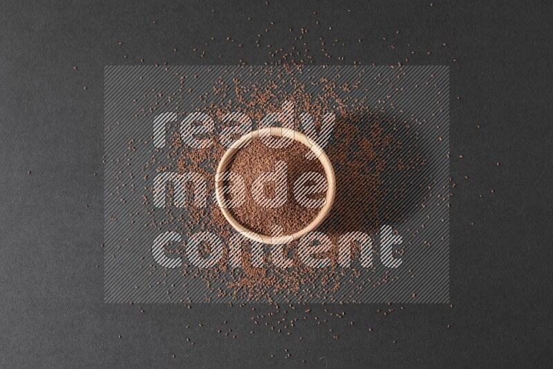 وعاء خشبي ممتلئ ببذور حب الرشاد محاط ببعض البذور علي خلفية سوداء