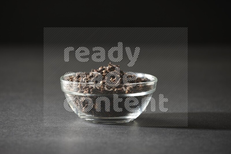 A glass bowl full of cloves on a black flooring