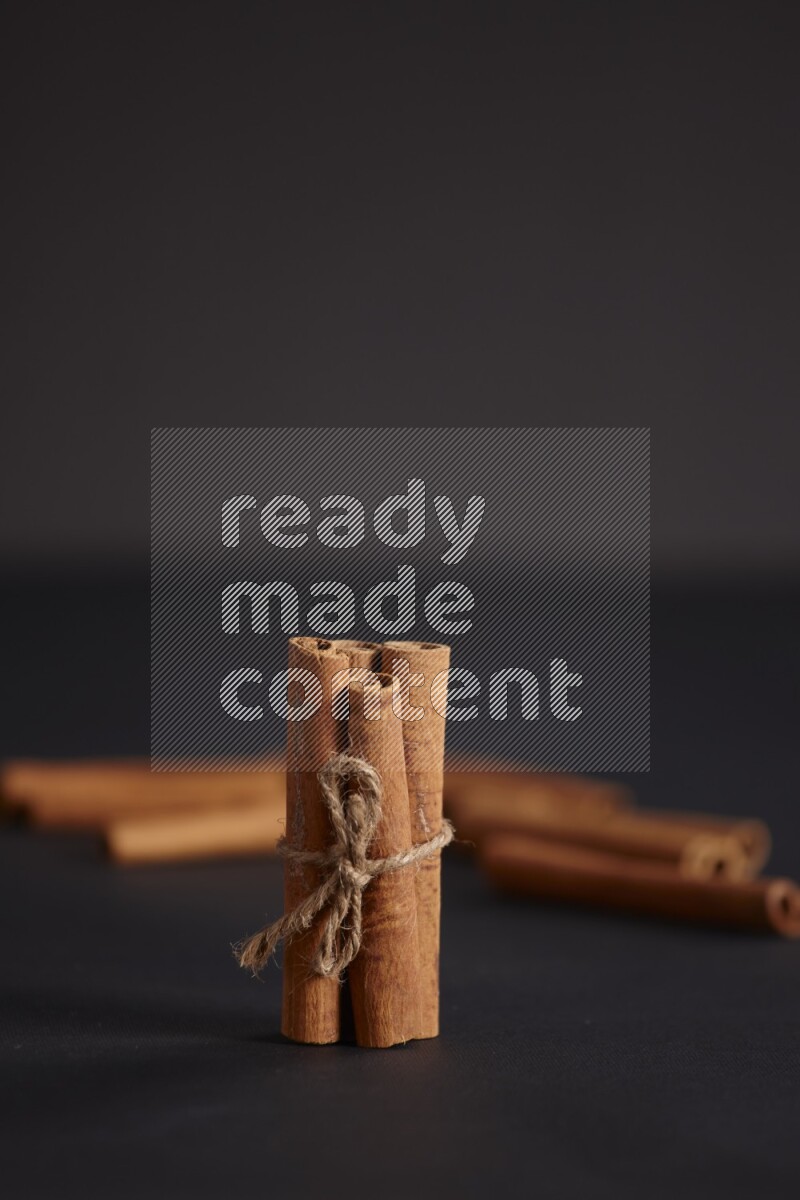 4 Cinnamon sticks stacked and bounded with more sticks in the background on black flooring