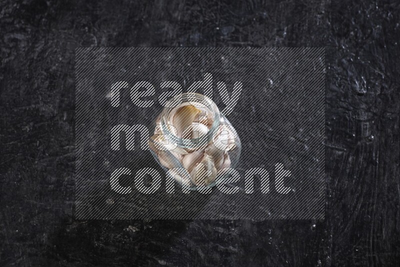 وعاء توابل زجاجي ممتلئ بفصوص الثوم علي خلفية سوداء