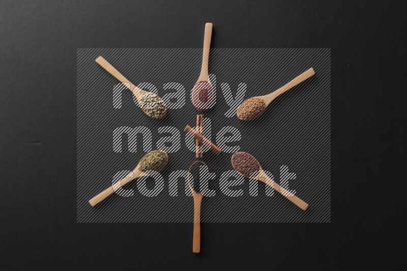 wooden spoons filled with white peppers, mustard seeds, black seeds, garden cress, cumin and flax on black flooring and shaped like a clock