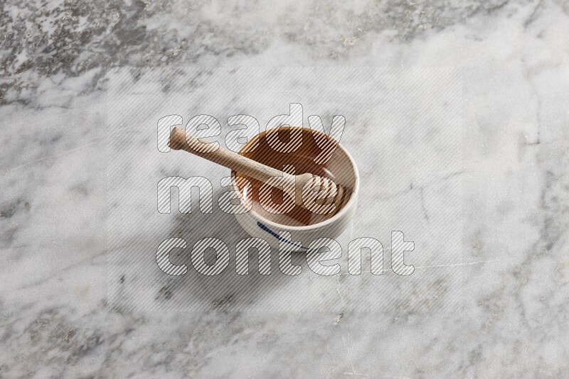 Multicolored pottery bowl with wooden honey dipper in it on grey marble background