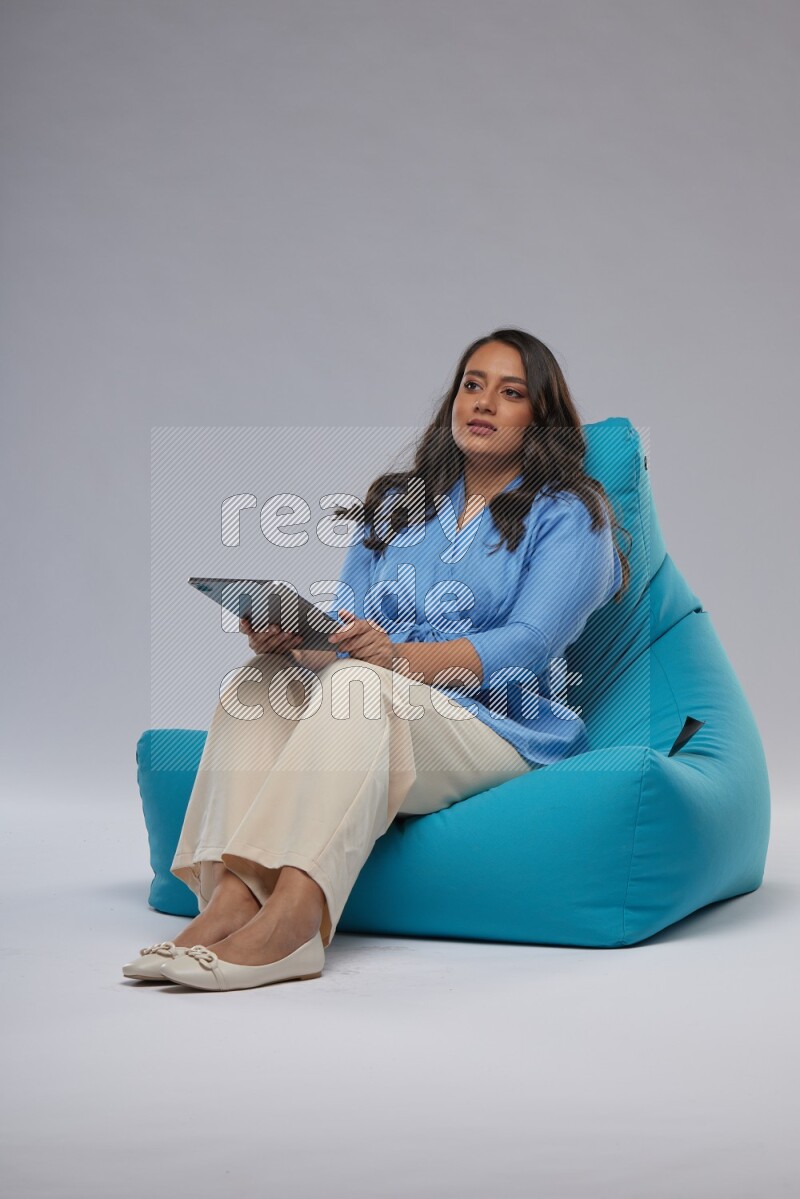 A woman sitting on a blue beanbag and working on tablet