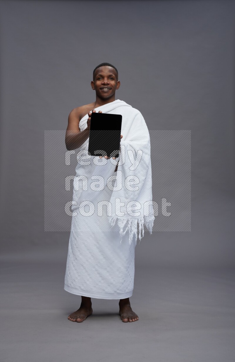 A man wearing Ehram Standing showing tablet to camera on gray background