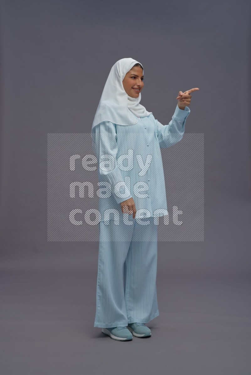 Saudi woman wearing hijab clothes standing interacting with the camera on gray background