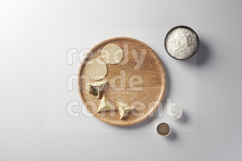 two closed sambosas and one open sambosa filled with meat while flour, salt, and black pepper aside in a wooden dish on a white background