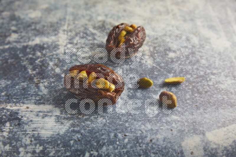 two pistachios stuffed madjoul dates on a rustic blue background