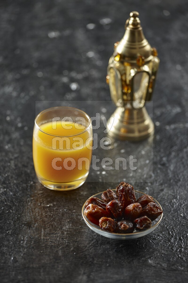 A golden lantern with different drinks, dates, nuts, prayer beads and quran on textured black background