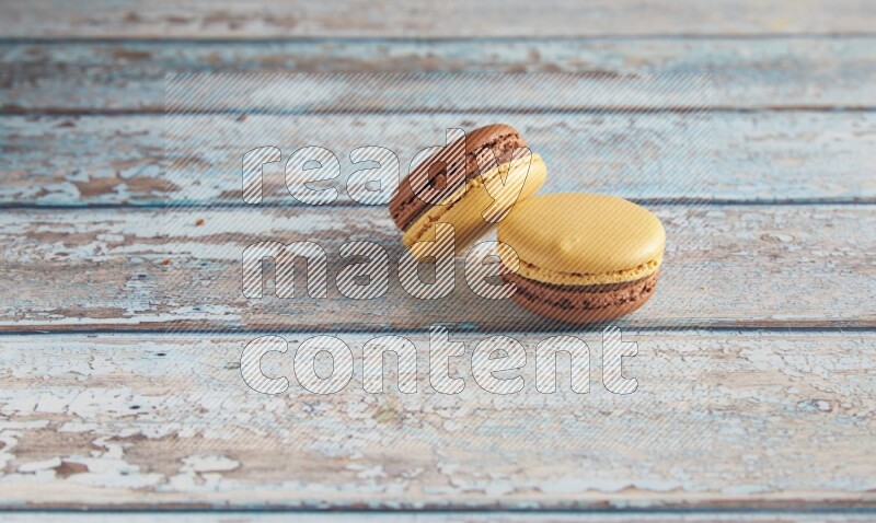 45º Shot of two Yellow and Brown Chai Latte macarons on light blue wooden background
