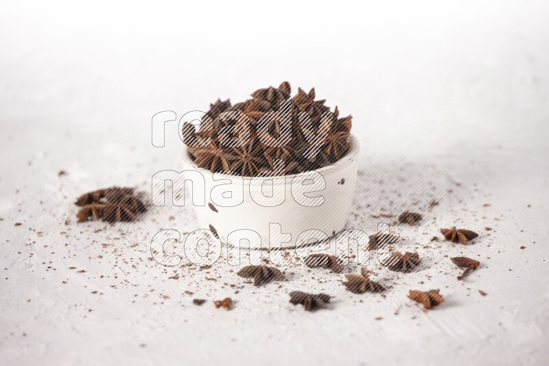 Star Anise in a white bowl and more of it sprinkled on white background