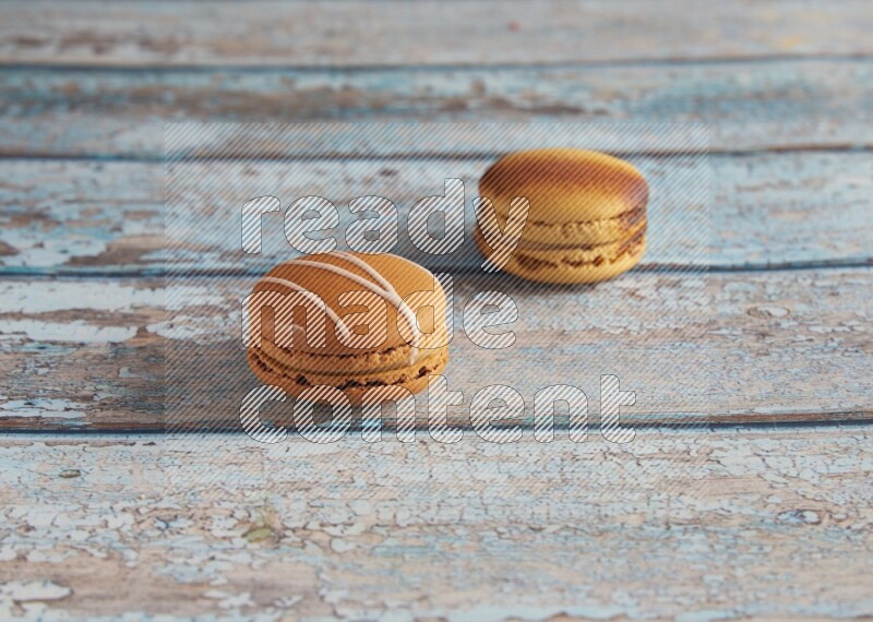 45º Shot of of two assorted Brown Irish Cream, and Yellow Crème Brulée macarons on light blue background