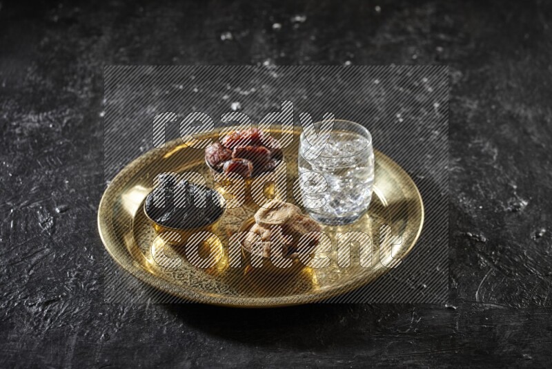 Dried fruits in metal bowls with water on a tray in dark setup