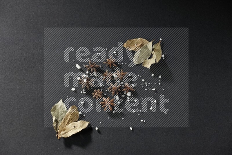 Salt, star anise and bay laurel on black flooring