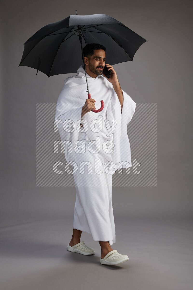 A man wearing Ehram Standing holding umbrella on gray background