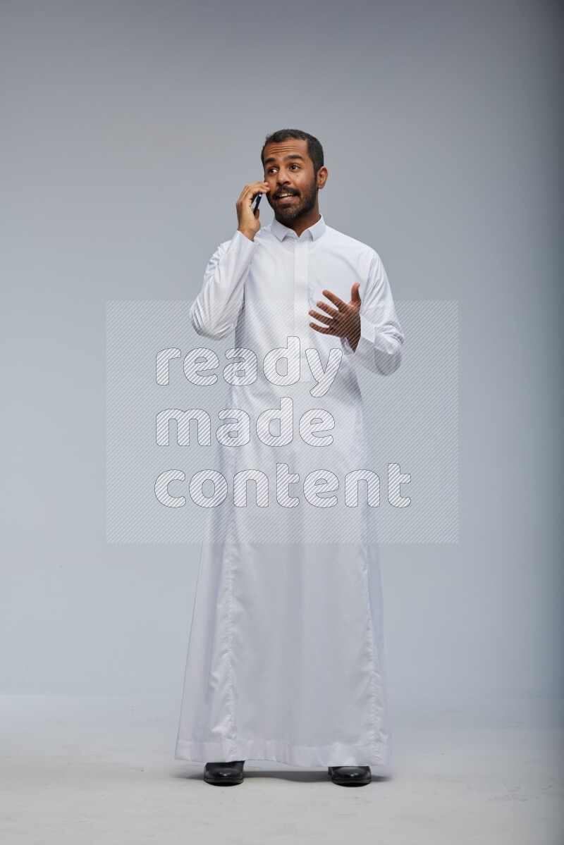 Saudi man wearing Thob standing talking on phone on Gray background