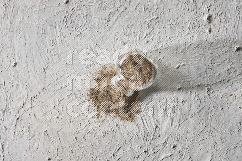 Flipped glass spice jar full of black pepper powder on a textured white flooring