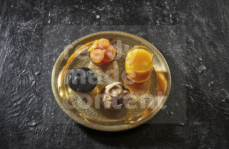 Dried fruits in metal bowls with qamar eldin on a tray in dark setup