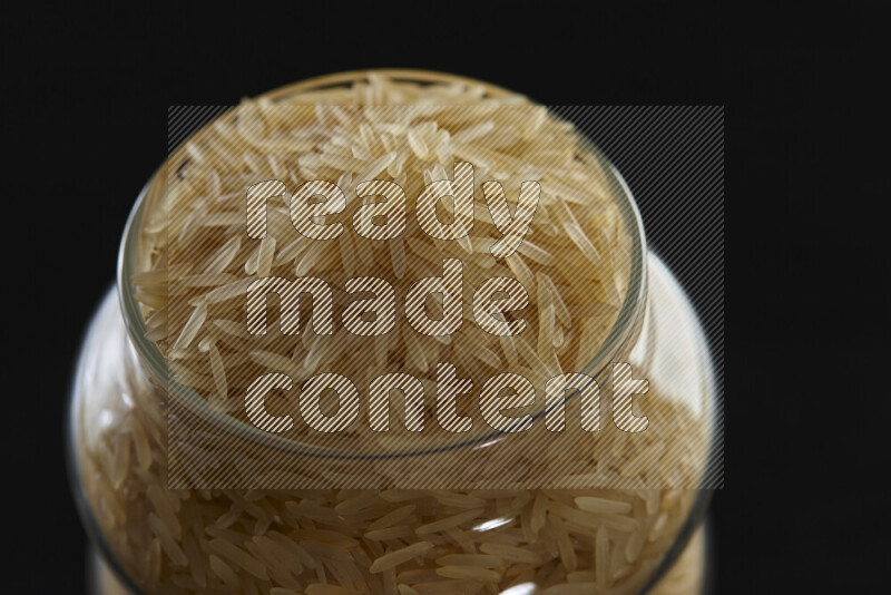 Basmati golden rice in a glass jar on black background