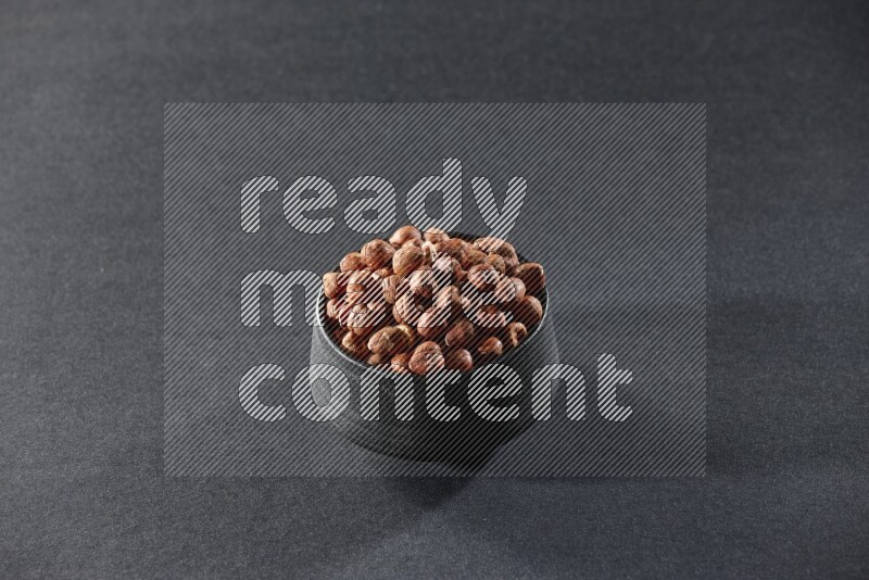A black pottery bowl full of peeled hazelnuts on a black background in different angles