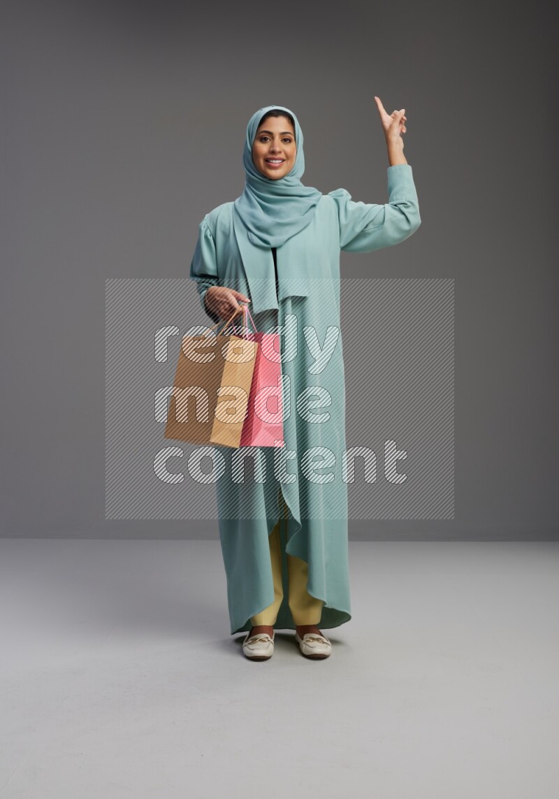 Saudi Woman wearing Abaya standing holding shopping bag on Gray background