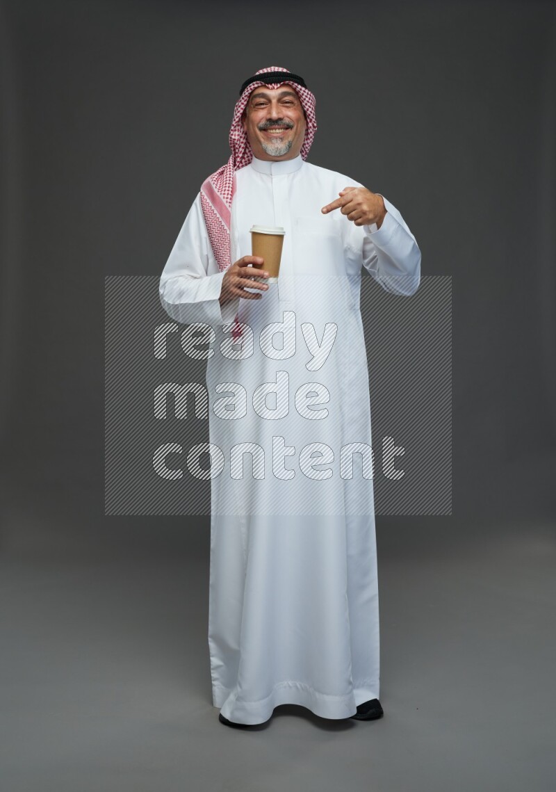 Saudi man with shomag Standing holding paper cup on gray background