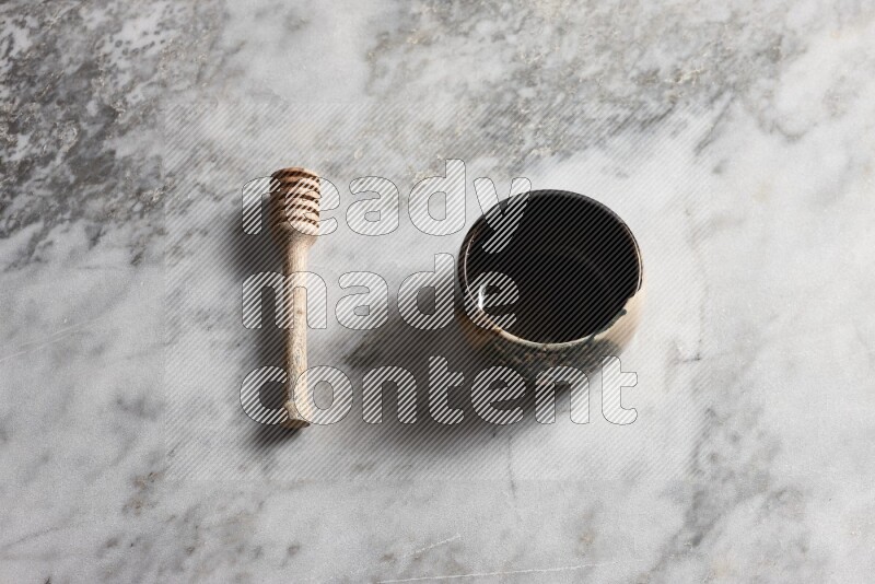 Multicolored pottery bowl with wooden honey dipper on the side on grey marble background