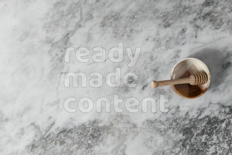 Multicolored pottery bowl with wooden honey dipper in it on grey marble background