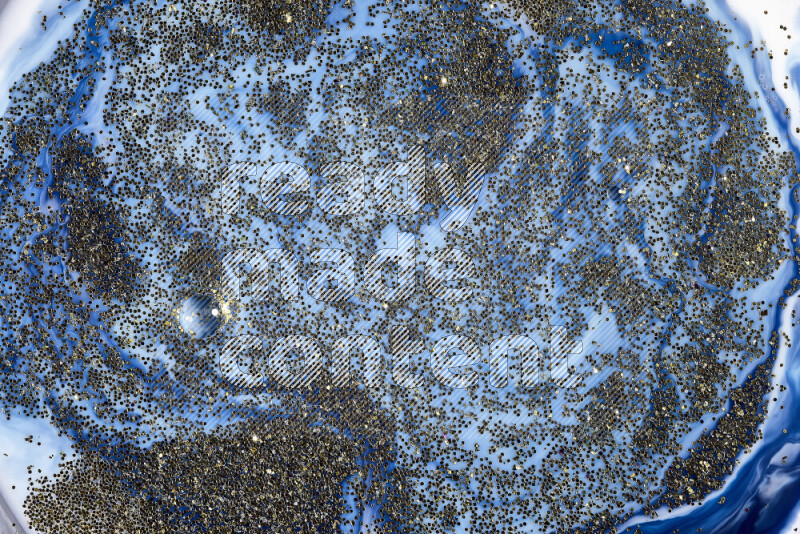 A close-up of sparkling gold glitter scattered on swirling blue background