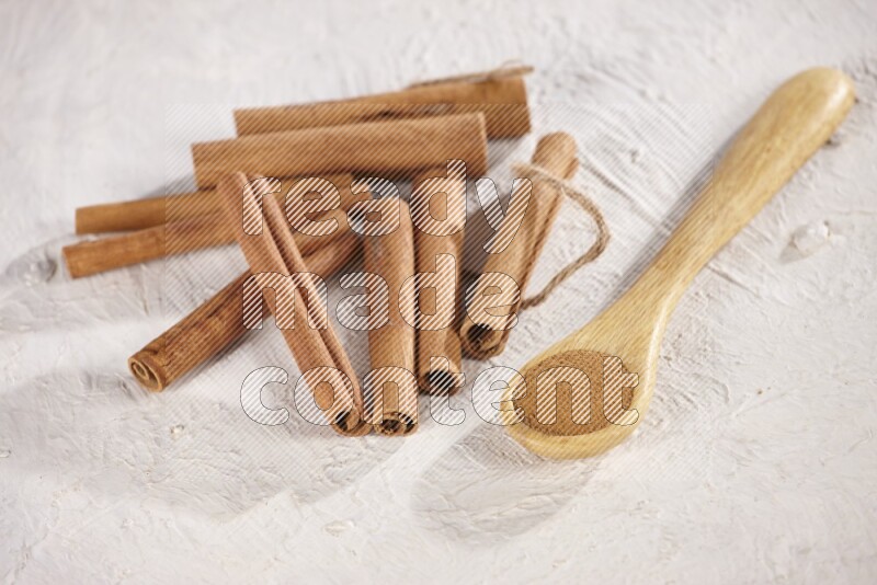 Cinnamon sticks stacked beside a wooden spoon full of cinnamon powder on white background