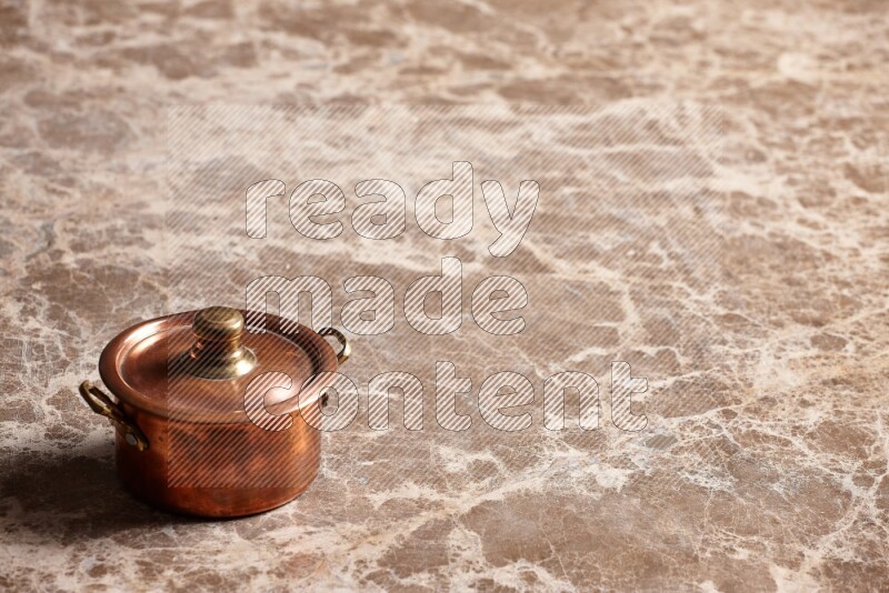 A small copper pot on beige marble background