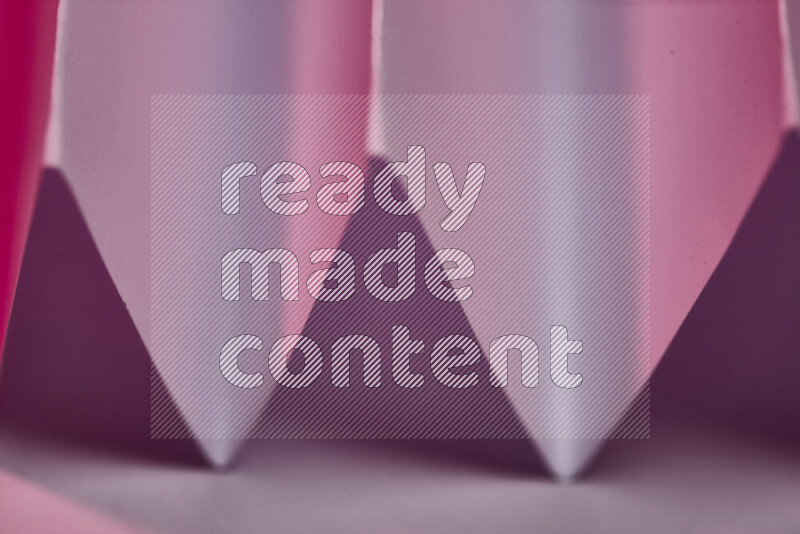 A close-up abstract image showing sharp geometric paper folds in pink gradients