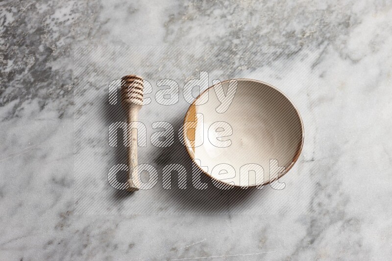 Multicolored pottery plate with wooden honey dipper on the side on grey marble background