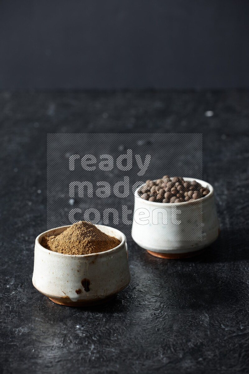 وعاءان بيج، أحدهما ممتلئ ببودرة بهار الفلفل الحلو والآخر بالحبوب على خلفية سوداء