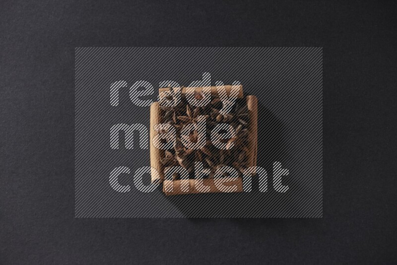 A single square of cinnamon sticks full of star anise on black flooring