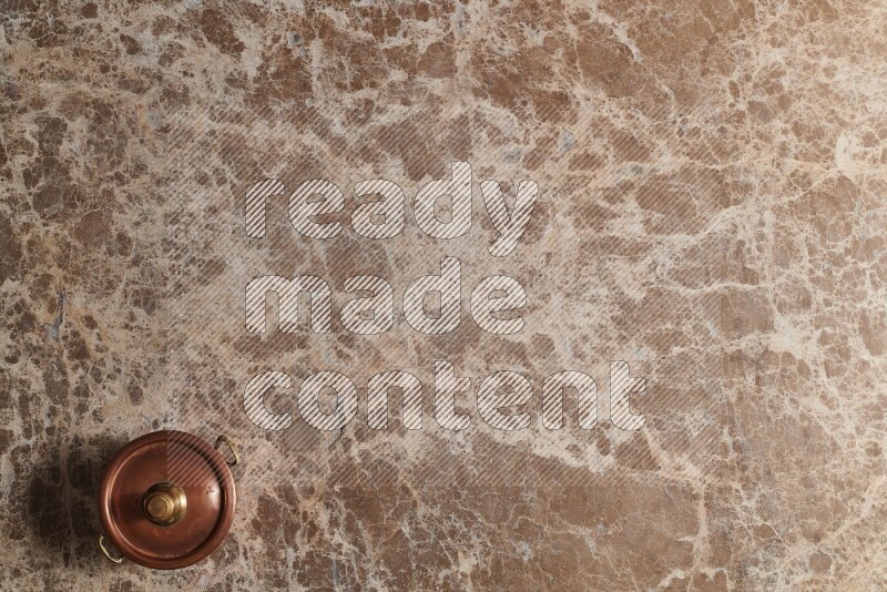 A small copper pot on beige marble background