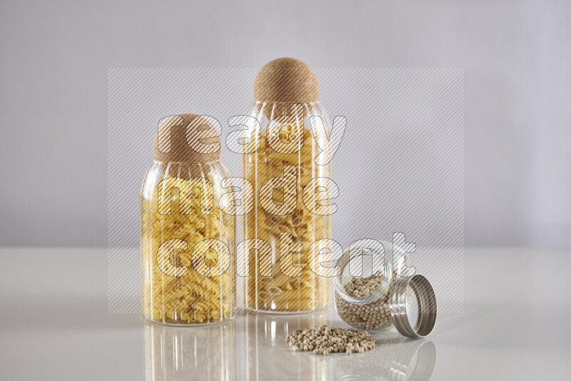 Raw pasta in glass jars with white peppers on light grey background