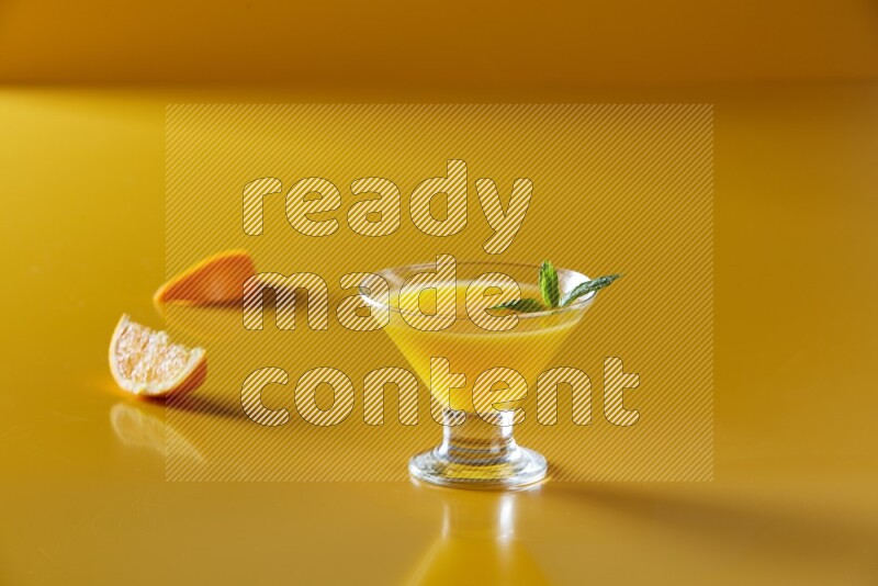 glass of orange juice with  mint on yellow background