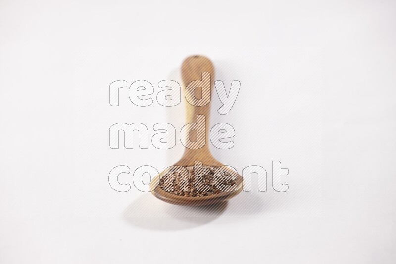 A wooden ladle full of flax seeds on a white flooring