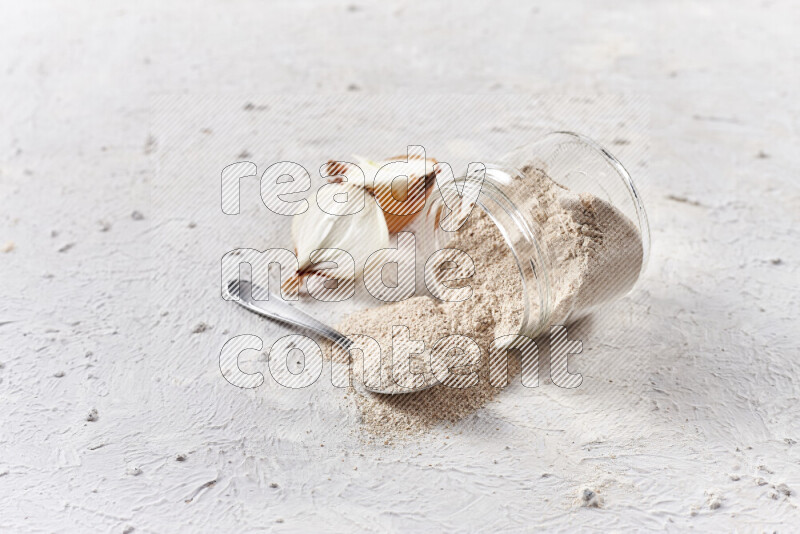 A glass jar full of onion powder flipped with some spilling powder on white background
