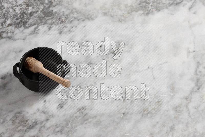 وعاء فخاري أسود مع ملعقة عسل خشبية بداخله على خلفية من الرخام الرمادي