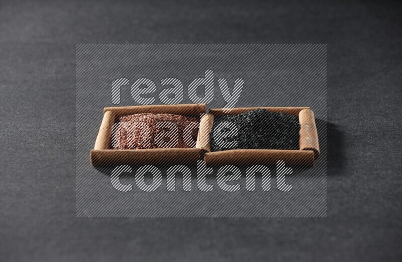 مربعان من أعواد القرفة ممتلئان بحب الرشاد وحبة البركة السوداء علي خلفية سوداء