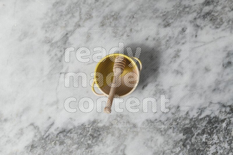 Multicolored pottery bowl with wooden honey dipper in it on grey marble background
