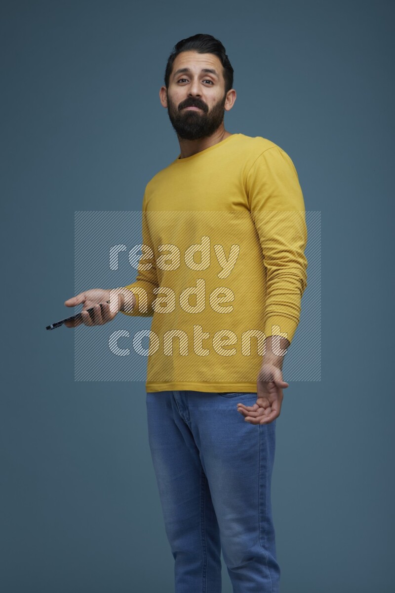 Man posing with a phone in a blue background wearing a yellow shirt