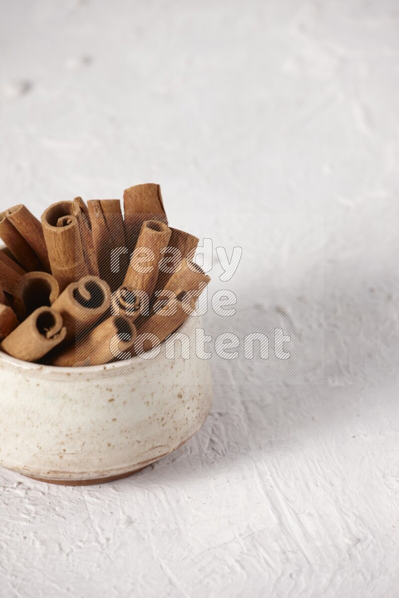 Cinnamon sticks in a beige bowl on a white background
