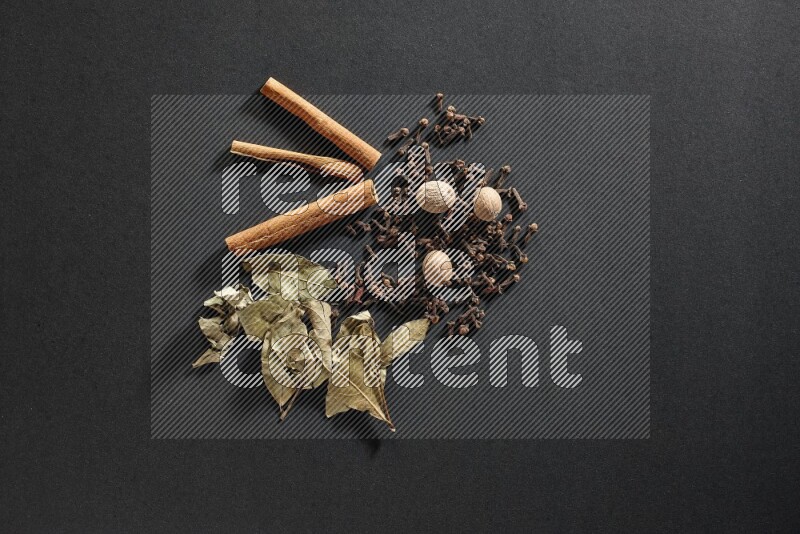 Cloves, ginger, bay laurel and cinnamon sticks on black flooring