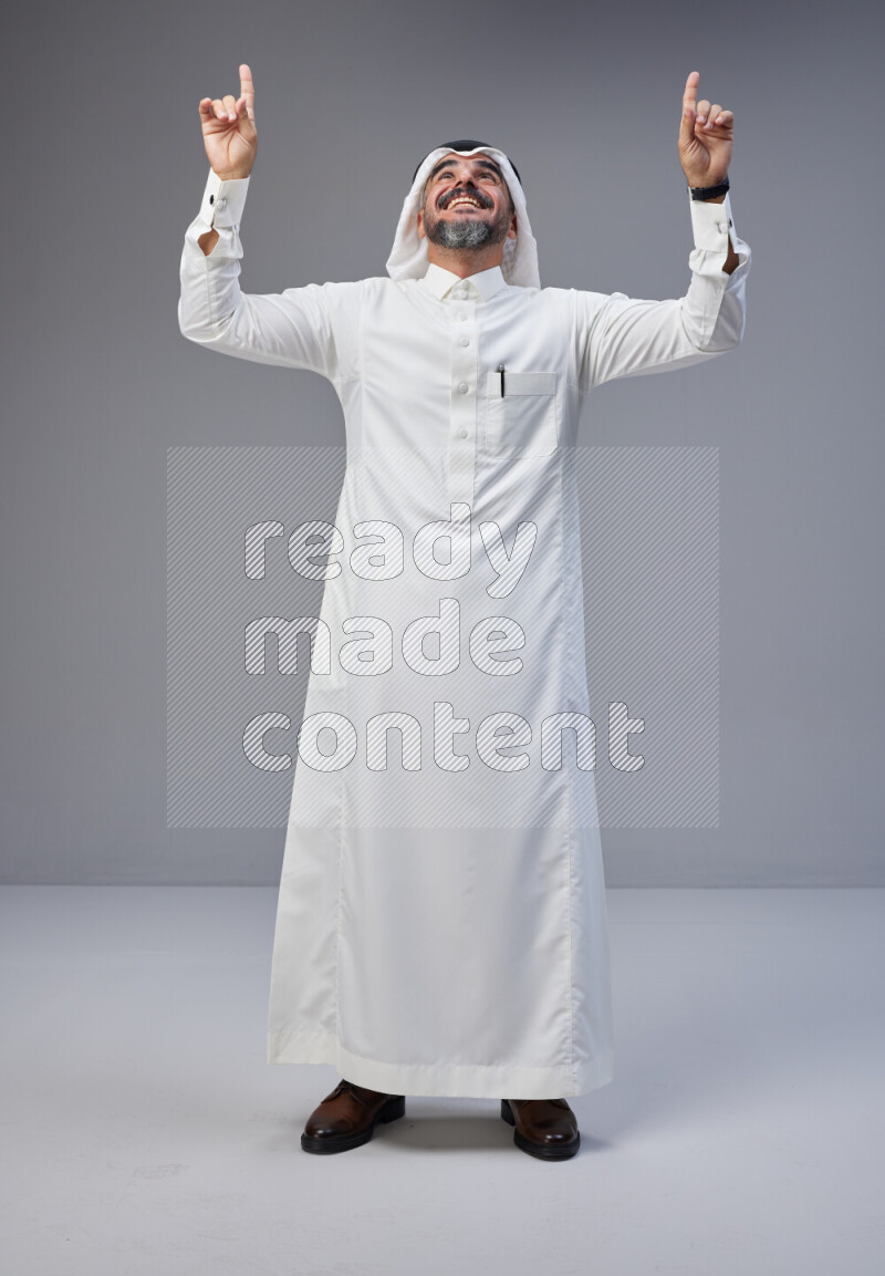 Saudi man Wearing Thob and white Shomag standing interacting with the camera on Gray background