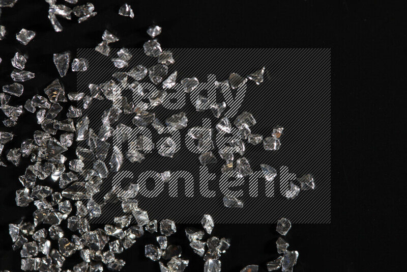 Silver shimmering fragments of glass scattered on a black background